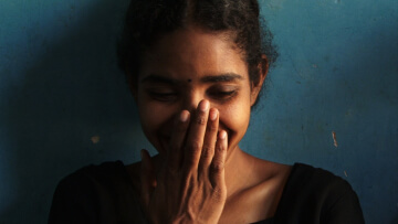 A woman covers her hand with her mouth while looking down