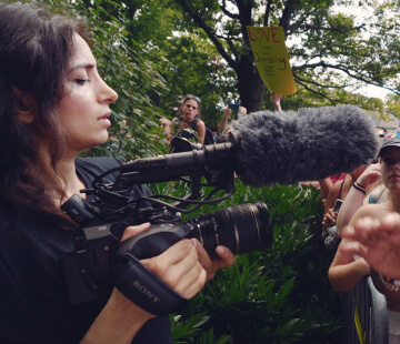 A woman looks through her camera's viewfinder while filming