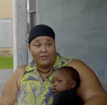 A Black woman holds her child while sitting on a porch