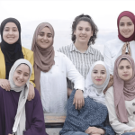A group of young hijabi women pose for a photo, smiling at the camera